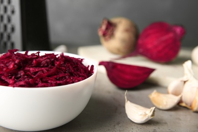 Photo of Bowl of grated fresh beets and garlic on table, closeup. Space for text