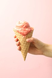 Photo of Woman holding waffle cone with delicious ice cream on pink background, closeup