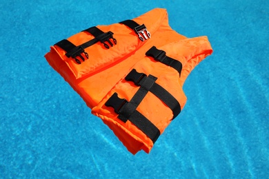 Photo of Bright orange life jacket floating in swimming pool