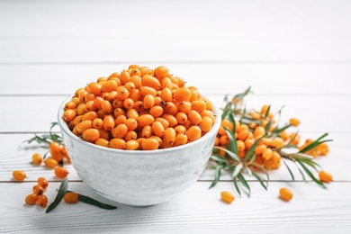 Photo of Fresh ripe sea buckthorn in bowl on white wooden table