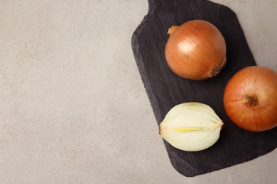 Photo of Slate board with ripe onions on grey table, top view. Space for text