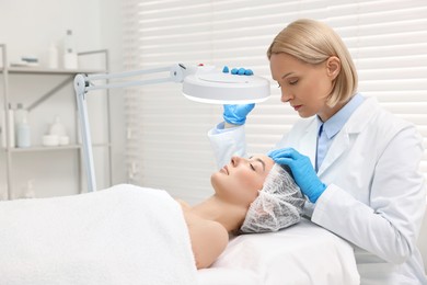 Photo of Dermatologist examining patient`s face under lamp in clinic