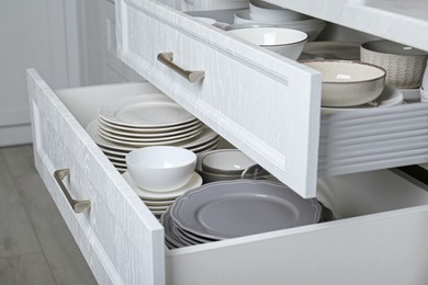 Photo of Open drawers with different plates and bowls in kitchen, closeup
