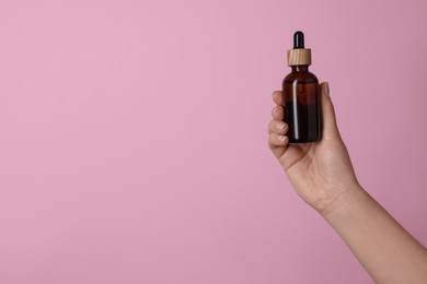 Photo of Woman holding bottle of cosmetic product on pink background, closeup. Space for text
