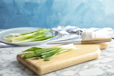 Photo of Board with wild garlic or ramson on marble table against color background. Space for text