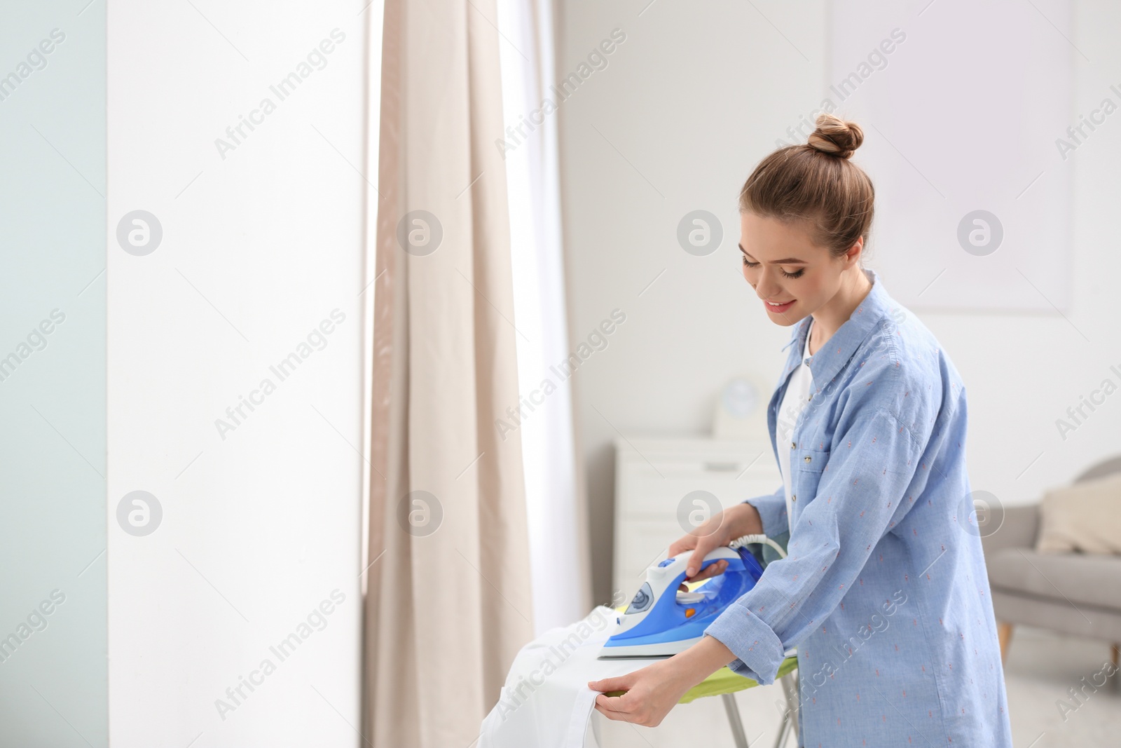 Young pretty woman ironing clean laundry indoors. Space for text Photo of Young pretty woman ironing clean laundry indoors. Space for text