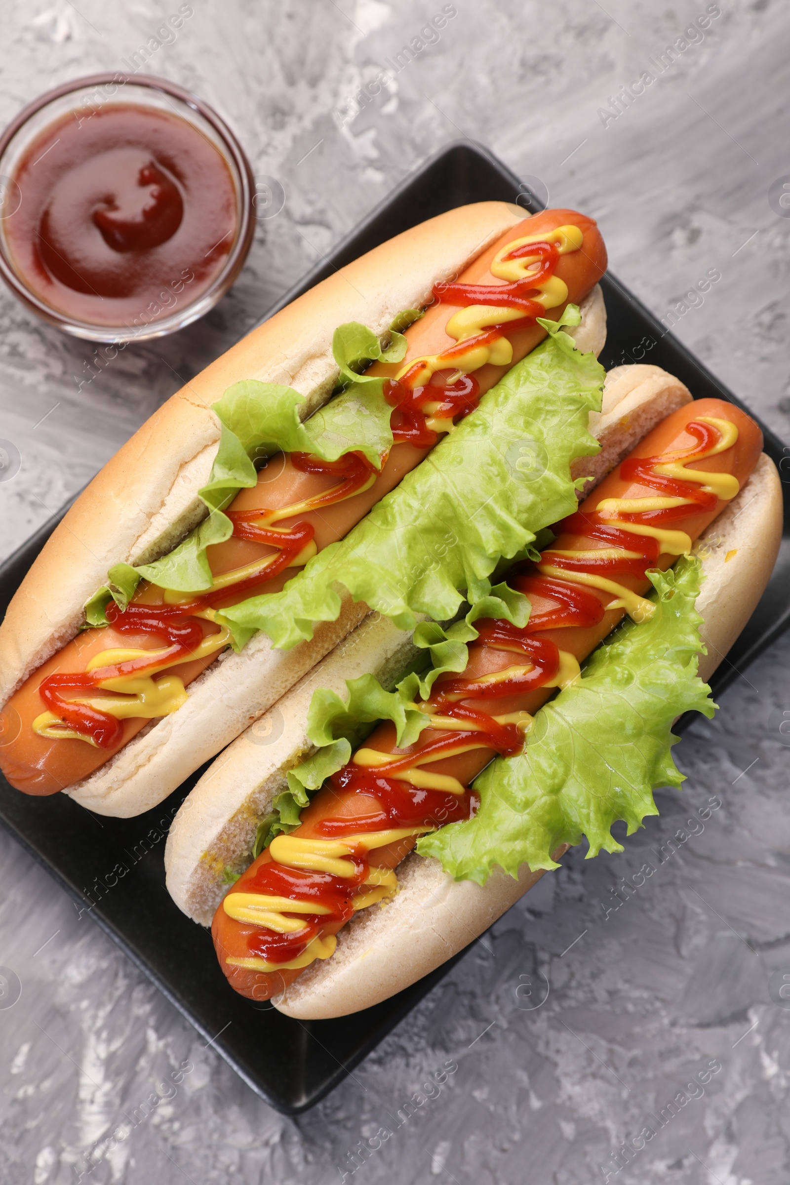 Photo of Tasty hot dogs with lettuce, ketchup and mustard on grey textured table, flat lay