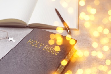 Image of Holy Bible, notebook and pen on stone table, bokeh effect