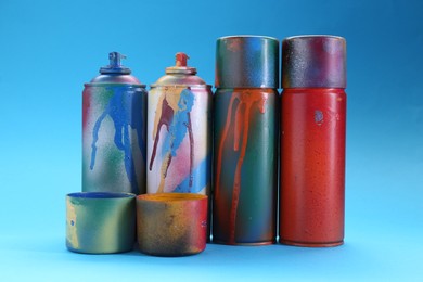Photo of Many spray paint cans with caps on light blue background