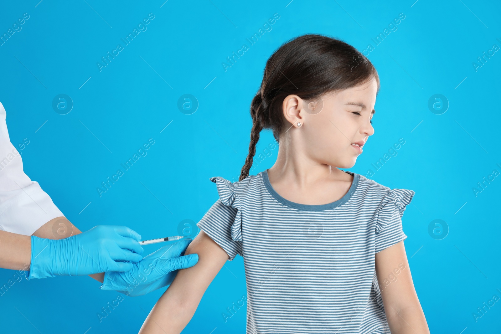 Photo of Doctor vaccinating little child on light blue background