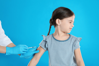 Doctor vaccinating little child on light blue background