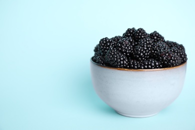 Photo of Fresh ripe blackberries in bowl on light blue background. Space for text
