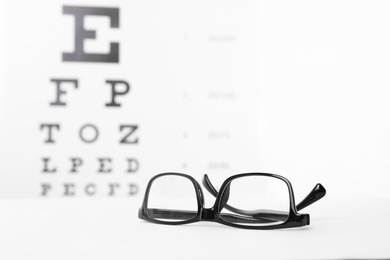 Photo of Glasses with corrective lenses on table against eye chart