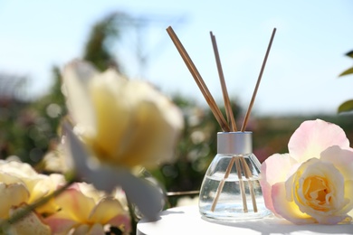 Reed air freshener with oil and fresh rose on table against blurred background. Space for text