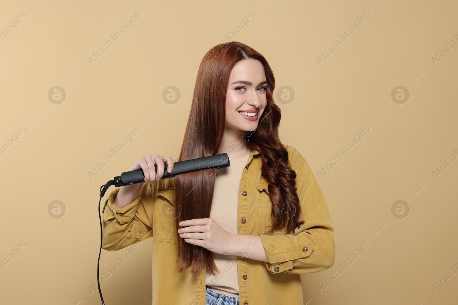 Photo of Beautiful woman using hair iron on beige background