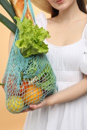 Photo of Woman with string bag of fresh vegetables and baguette on beige background, closeup