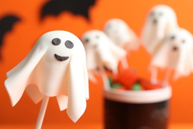 Photo of Delicious Halloween themed cake pops on orange background, closeup. Space for text