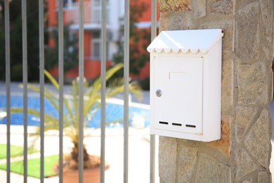 Photo of White metal letter box on stone column near fence outdoors