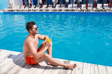 Handsome young man with refreshing cocktail near swimming pool on sunny day. Space for text