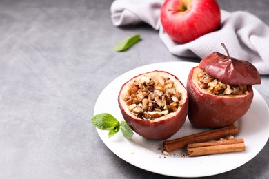 Tasty baked apples with nuts, honey, cinnamon sticks and mint on gray table, space for text