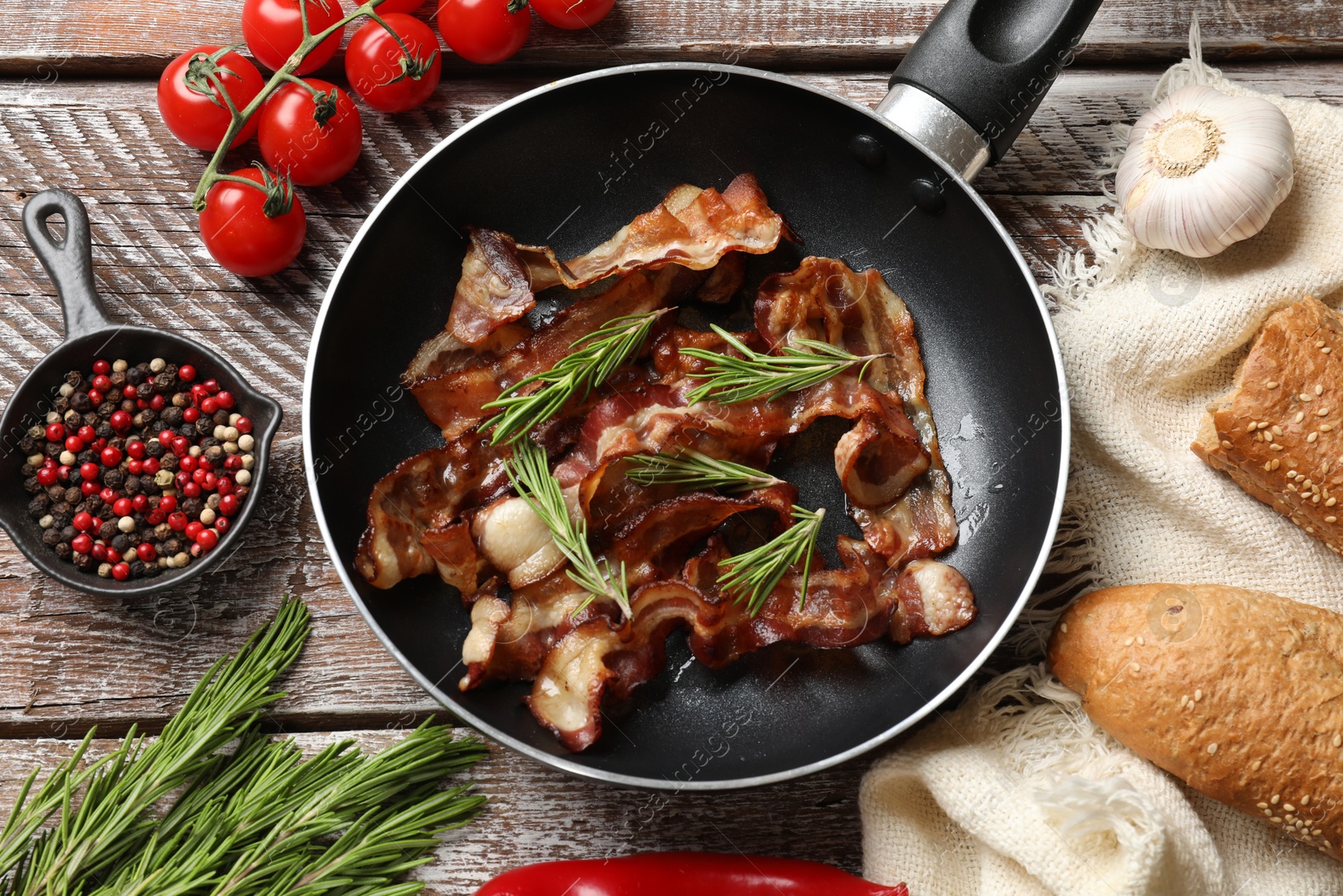 Photo of Delicious bacon slices in frying pan and products on wooden table, flat lay