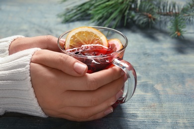 Photo of Woman holding cup with red mulled wine on table, closeup