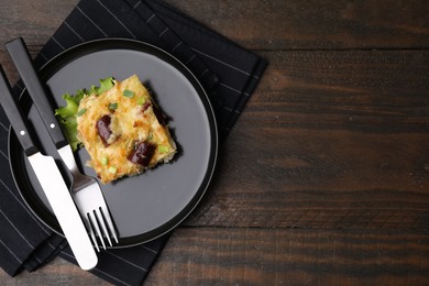 Photo of Tasty sausage casserole with green onions and cutlery served on wooden table, top view. Space for text