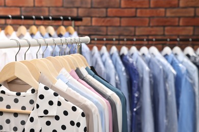 Photo of Dry-cleaning service. Many different clothes hanging on rack against brick wall, closeup