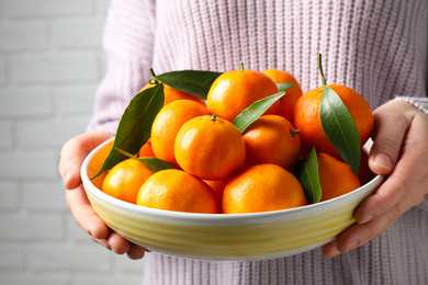 Photo of Woman holding bowl of tangerines, closeup. Juicy citrus fruit