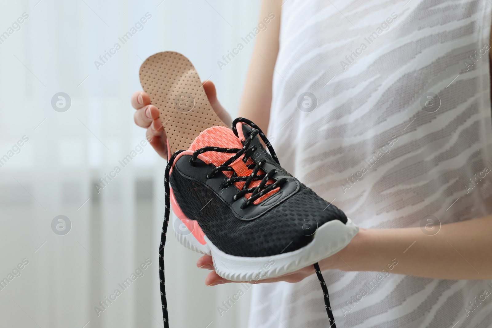 Photo of Woman putting orthopedic insole into shoe indoors, closeup. Foot care