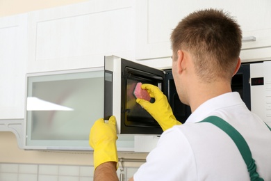 Male janitor cleaning microwave oven in kitchen