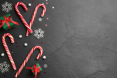 Photo of Flat lay composition with candy canes and Christmas decor on black table. Space for text