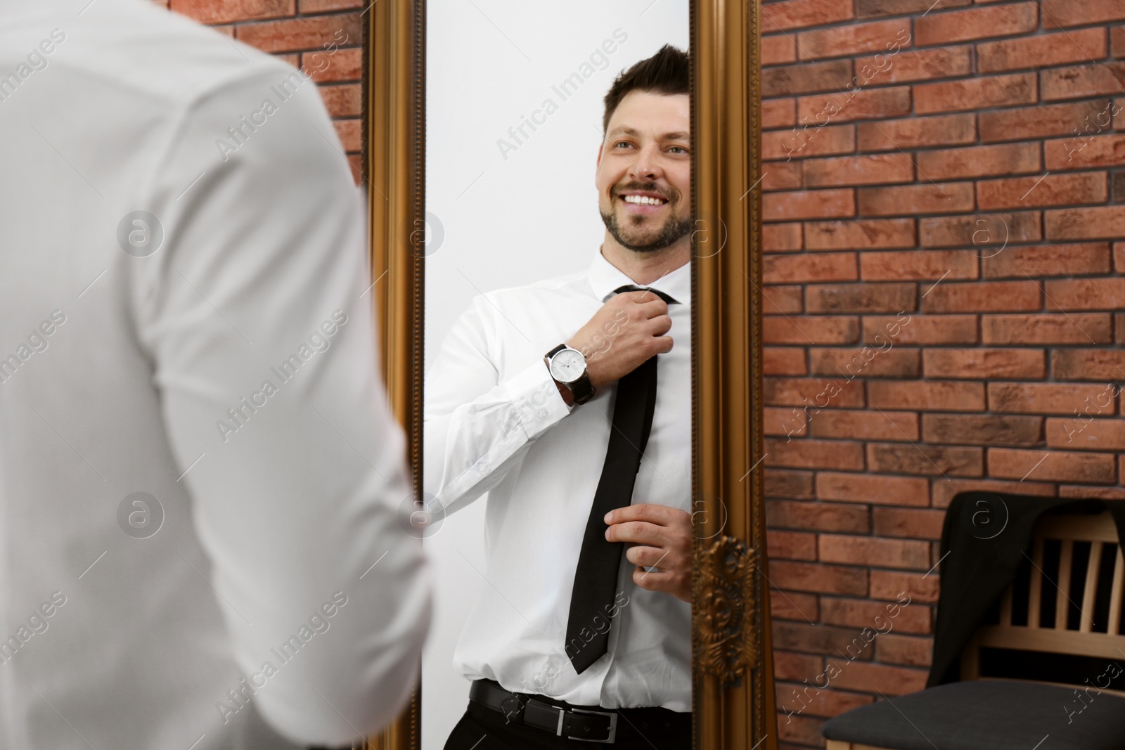 Photo of Confident man adjusting necktie near mirror in room