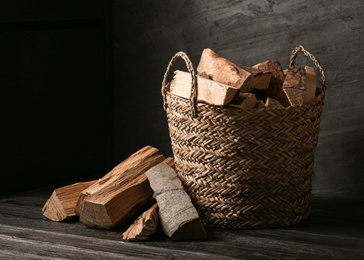Photo of Wicker basket with cut firewood on black table