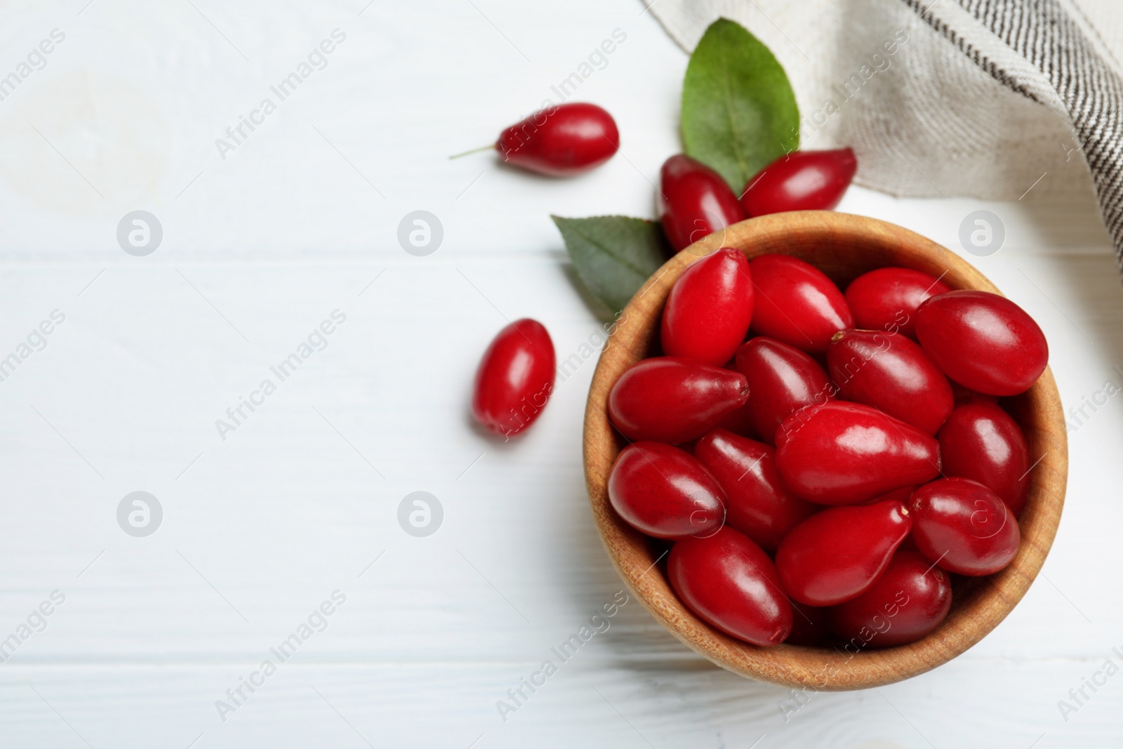 Photo of Fresh ripe dogwood berries with green leaves on white wooden table, flat lay. Space for text