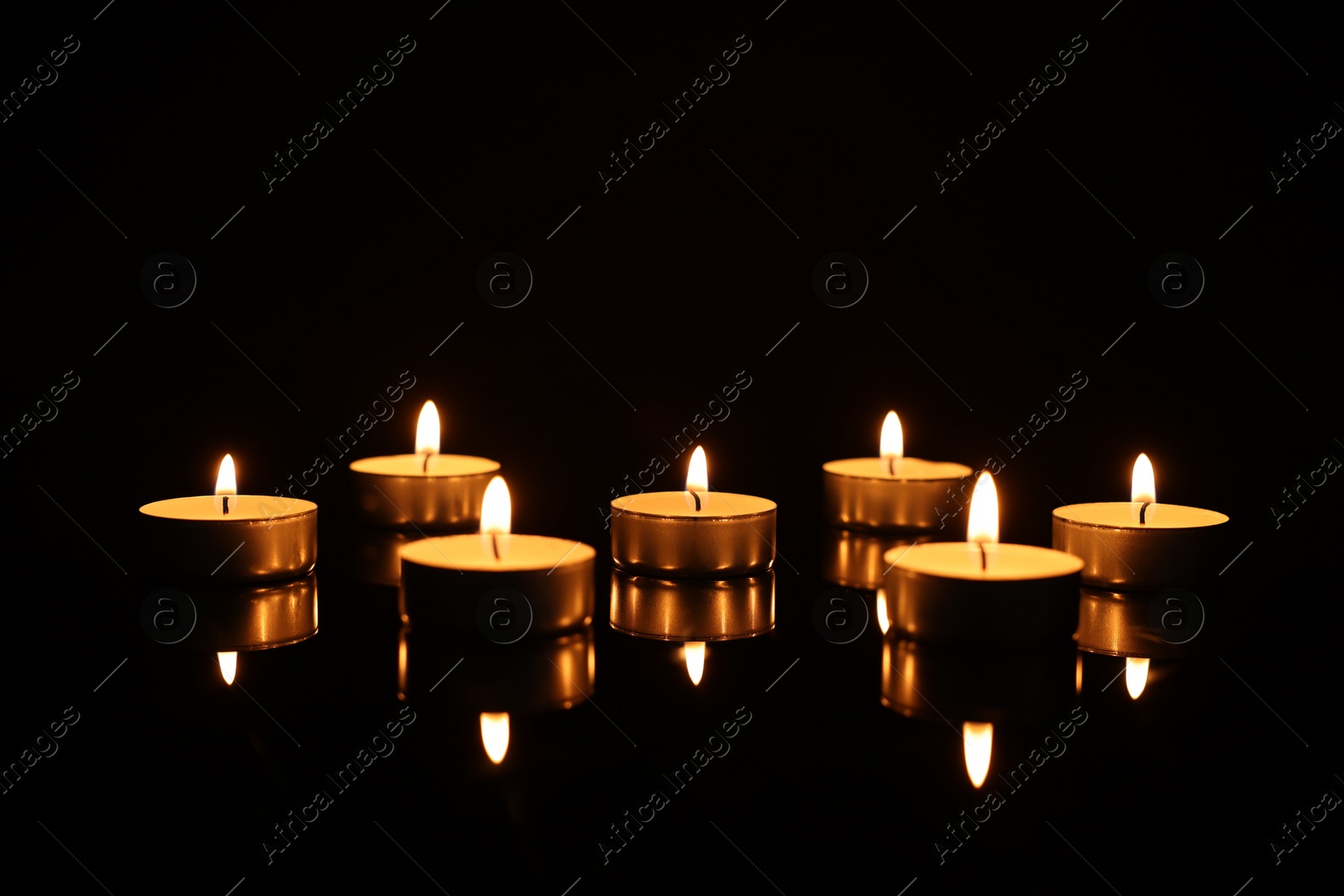 Photo of Burning candles on mirror surface in darkness