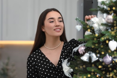 Smiling woman decorating Christmas tree in room