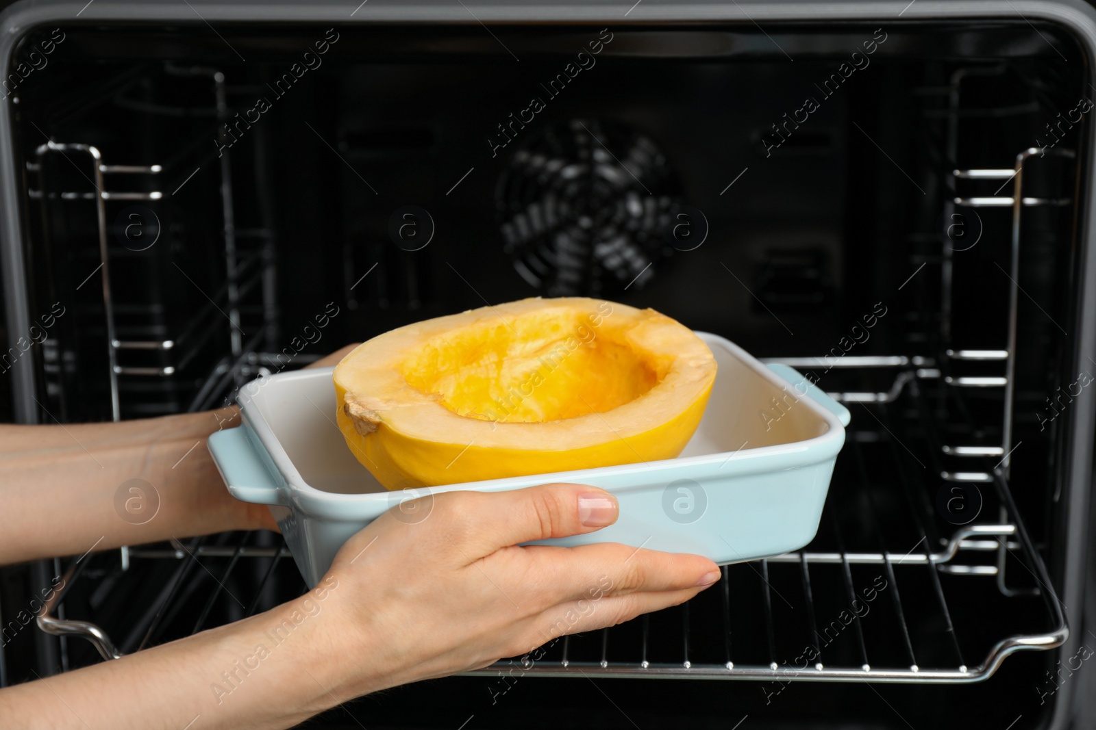 Photo of Woman putting half of fresh spaghetti squash into oven, closeup