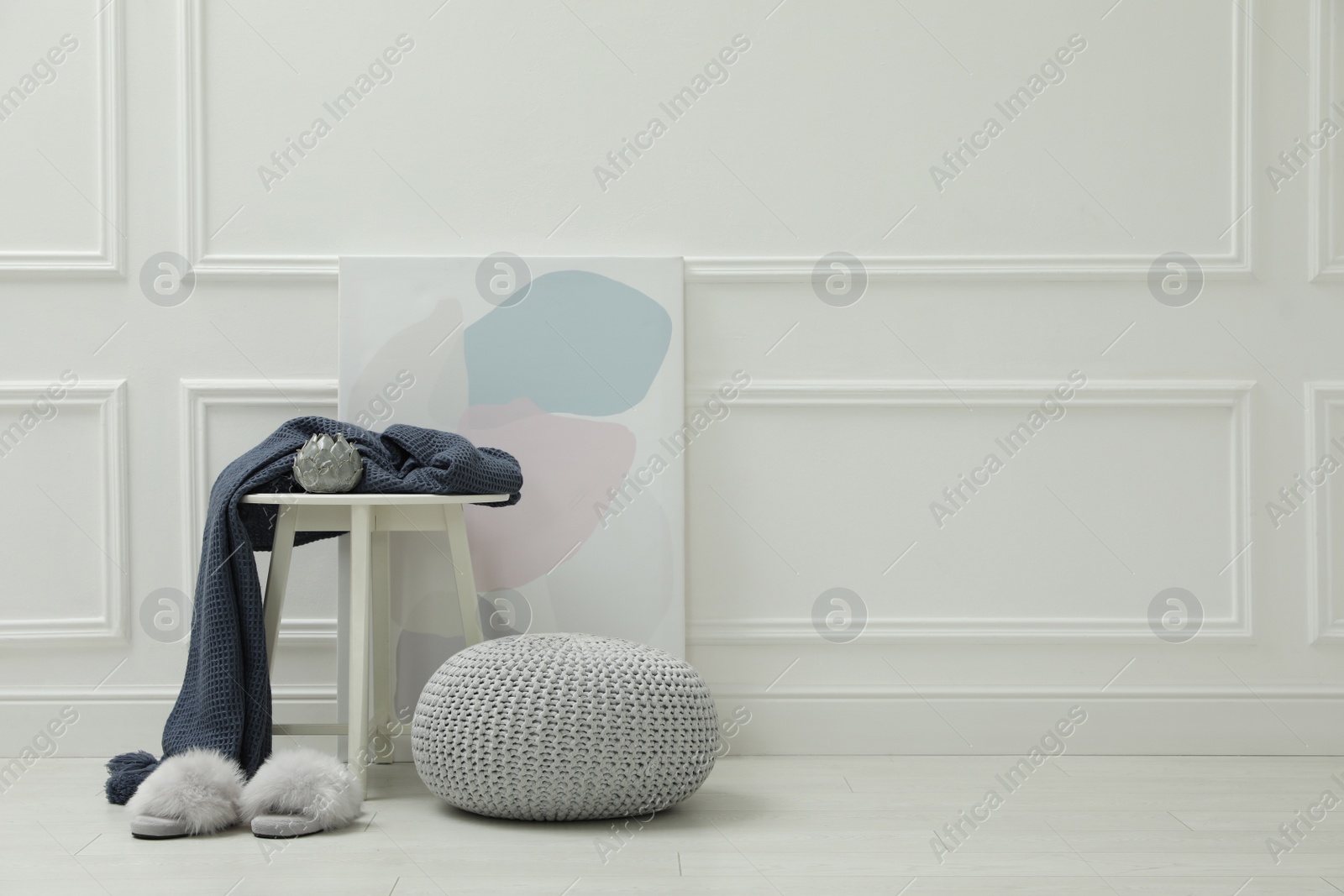 Photo of Knitted pouf, fuzzy slippers and decor elements near white wall indoors. Space for text