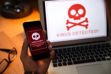 Photo of Man holding smartphone with warning about virus attack at table, closeup