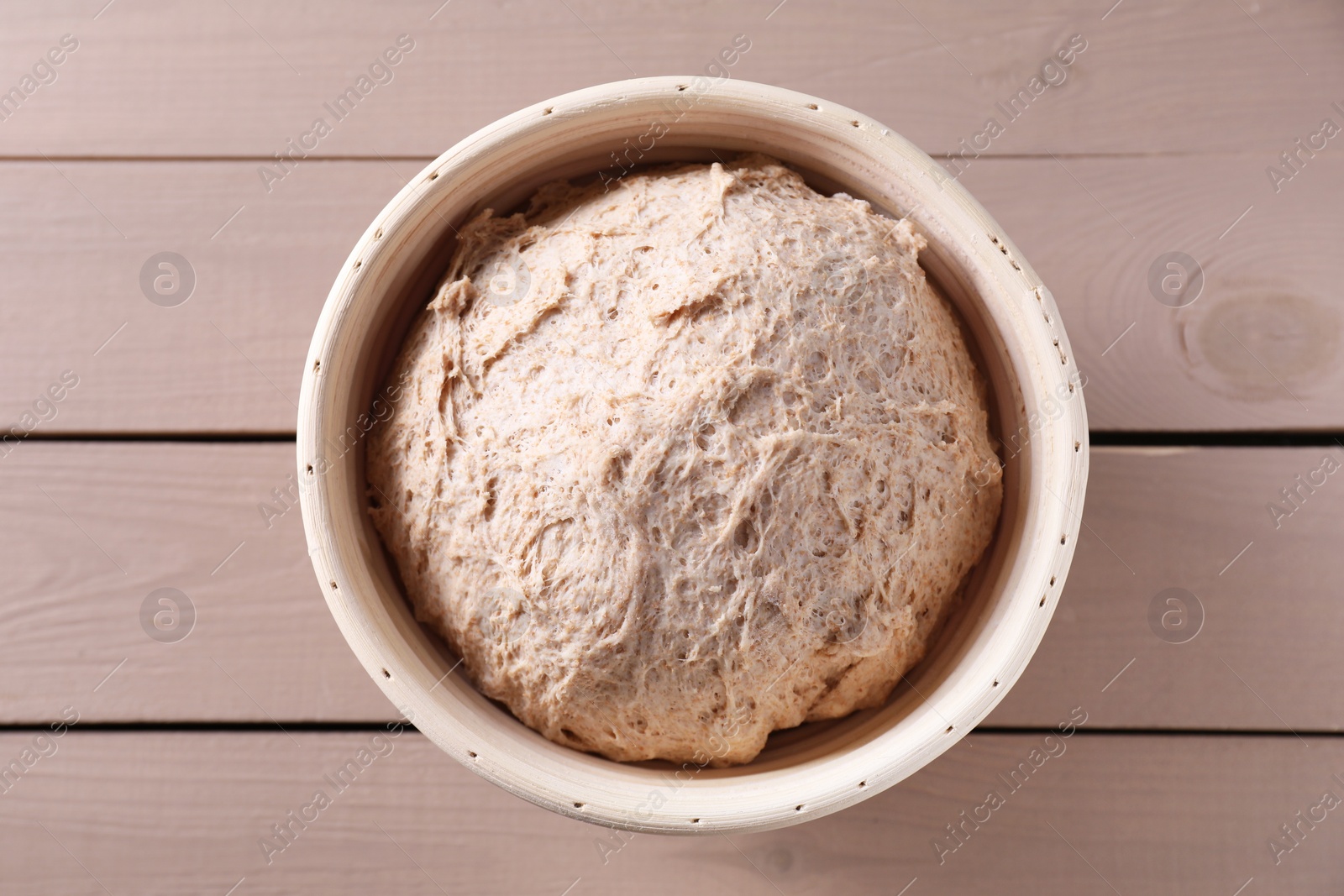 Photo of Fresh sourdough in proofing basket on wooden table, top view