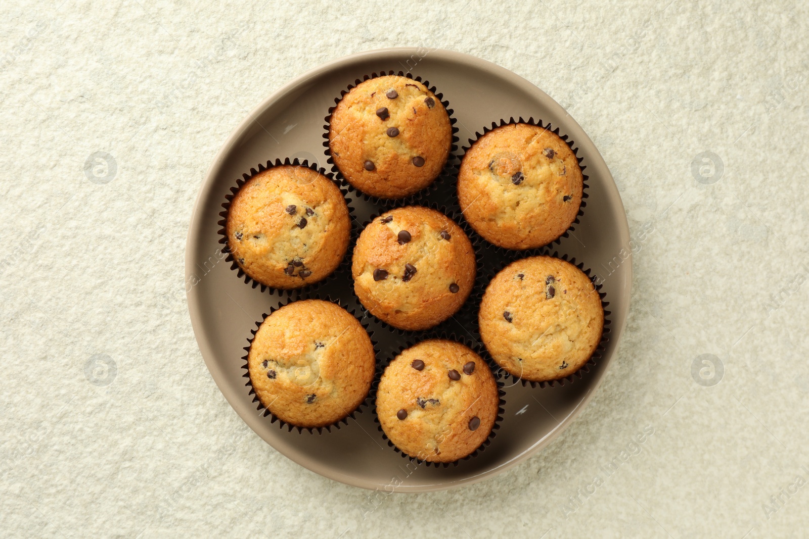 Photo of Delicious sweet muffins with chocolate chips on light textured table, top view