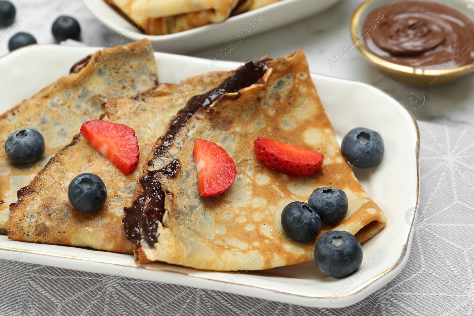 Photo of Tasty crepes with chocolate paste and berries served on table, closeup