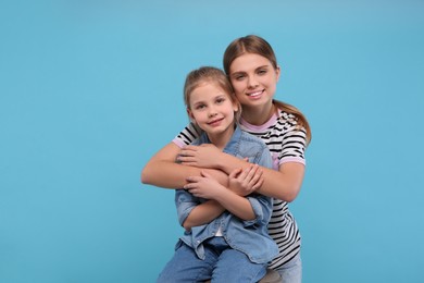 Photo of Young woman hugging her little daughter on light blue background, space for text. Happy Mother's Day