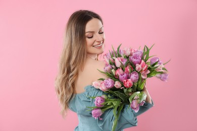 Happy young woman with bouquet of beautiful tulips on pink background