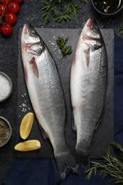 Photo of Fresh raw sea bass fish and ingredients on black table, flat lay