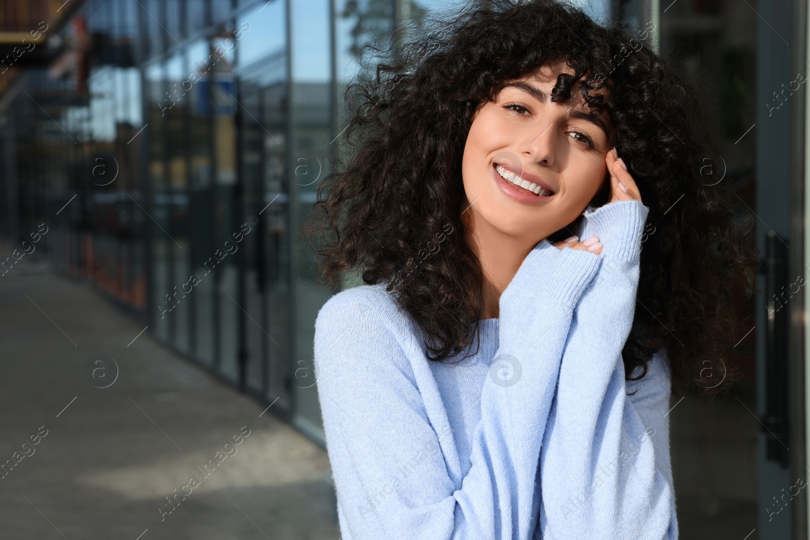 Photo of Happy young woman in stylish light blue sweater outdoors, space for text