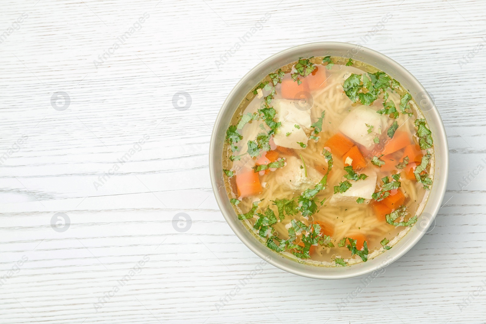 Photo of Bowl of fresh homemade chicken soup on wooden background, top view with space for text