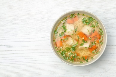 Bowl of fresh homemade chicken soup on wooden background, top view with space for text