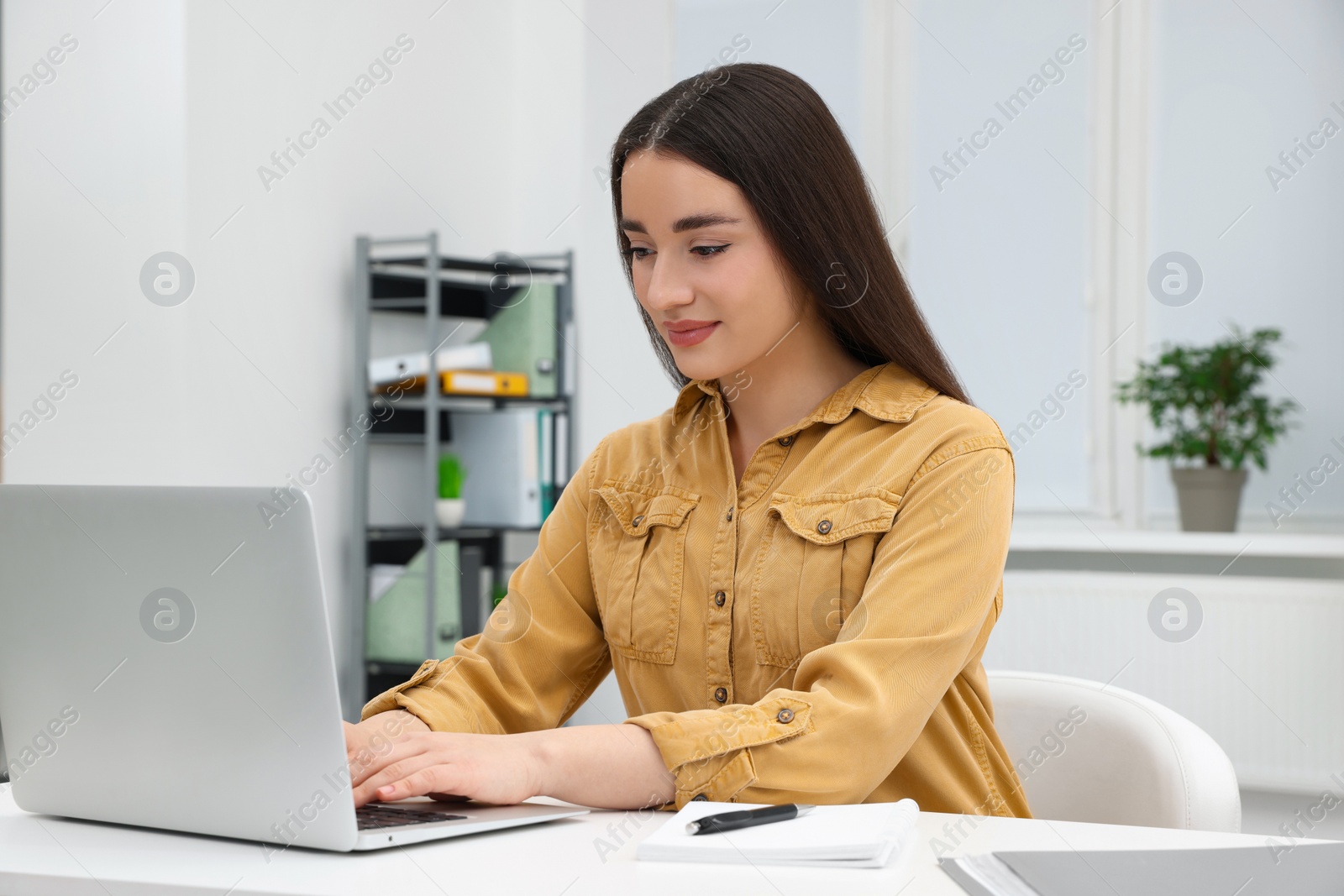 Photo of Young female intern working with laptop at table in office